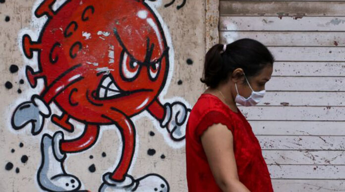Woman walks past a coronavirus-themed graffiti on a street in Mumbai