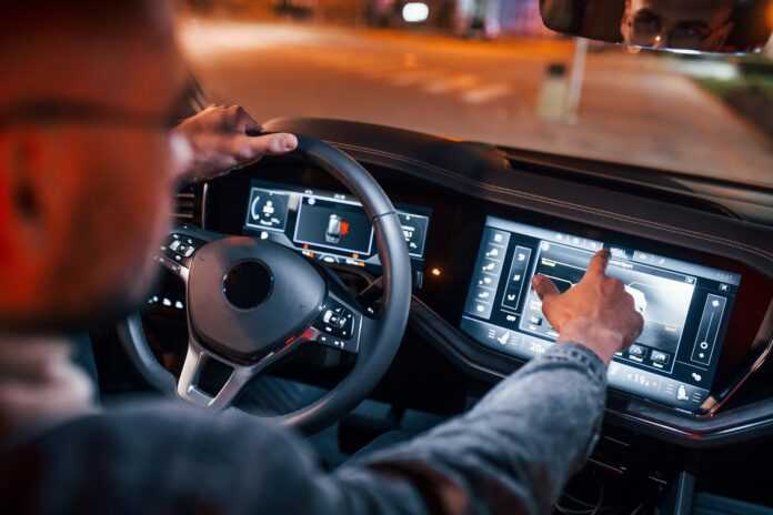 Using navigation display. Handsome unshaved man in fashionable clothes riding his automobile