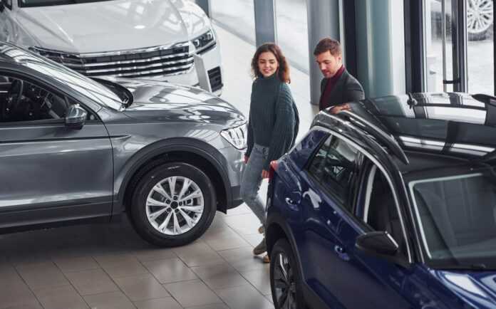 Professional salesman assisting young girl by choosing new modern automobile indoors